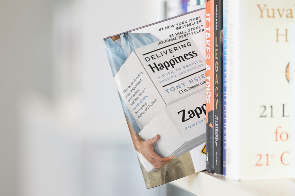 Delivering Happiness book is photographed on a book shelf. 