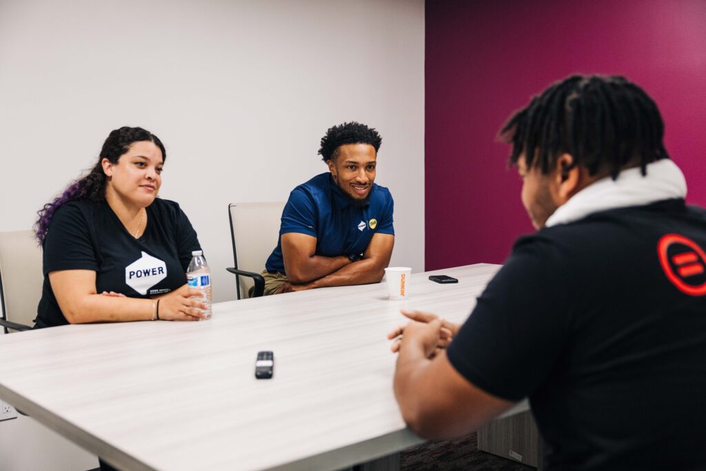 Two POWER B.E.R.G. members sit across a table from a recent high school graduate, providing career advice. 