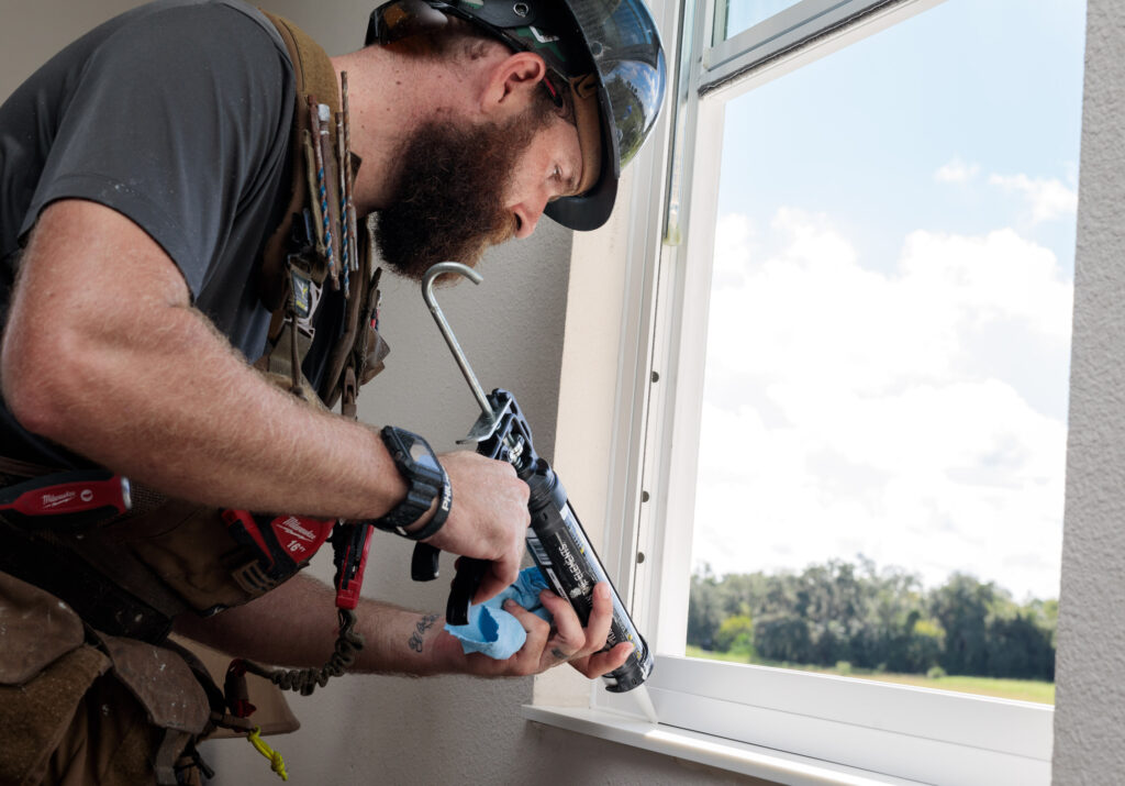 A POWER craftsman caulking a window.