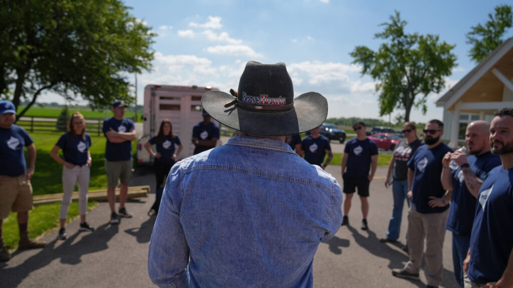 POWER employees stand in a circle to listen to opening remarks from a BraveHearts staff member ahead of their volunteer activity.